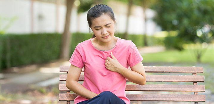 Junge Frau sitzt auf einer Bank und fasst sich an die Brust
