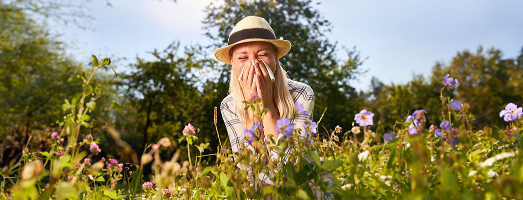 Junge Frau befindet sich auf Blumenwiese und muss niesen