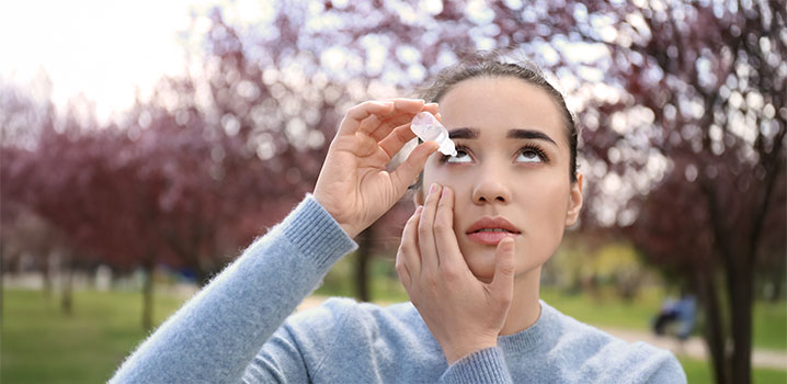 Junge Frau im Freien lehnt Kopf nach hinten und tropft sich Augentropfen ins Auge