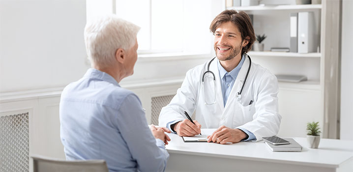 Ältere Frau sitzt einem jungen Arzt in Kittel gegenüber