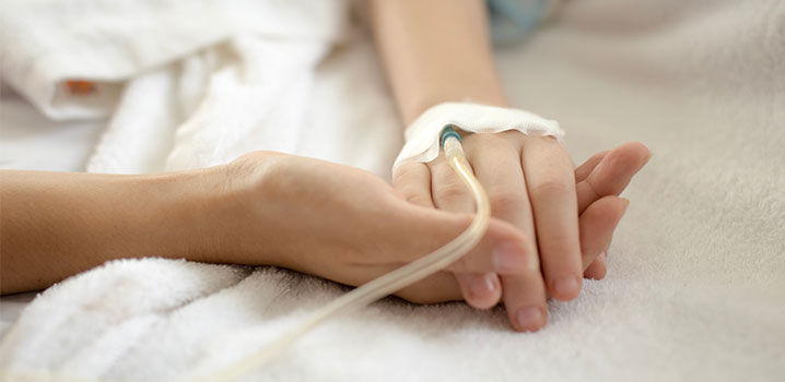 Eine Hand mit Kanüle liegt in einer gesunden Hand