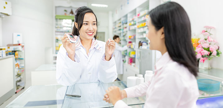 Eine Apothekerin zeigt einer Kundin am Tresen ein Blutzucker-Messgerät