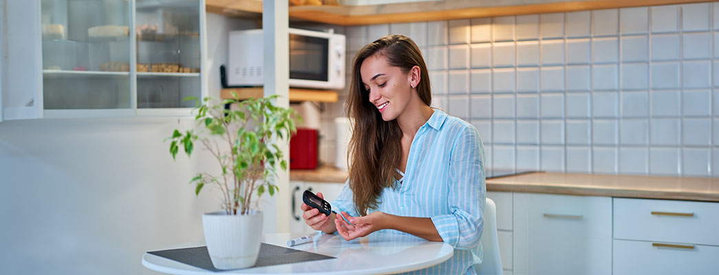 Junge Frau sitzt am Küchentisch und misst ihren Blutzucker