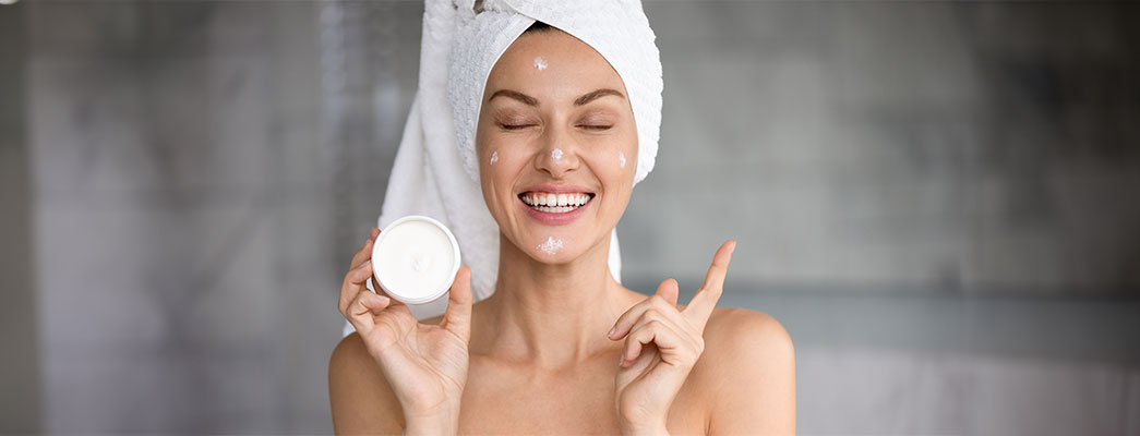 Frau mit Handtuch auf dem Kopf und Cremedose in der Hand