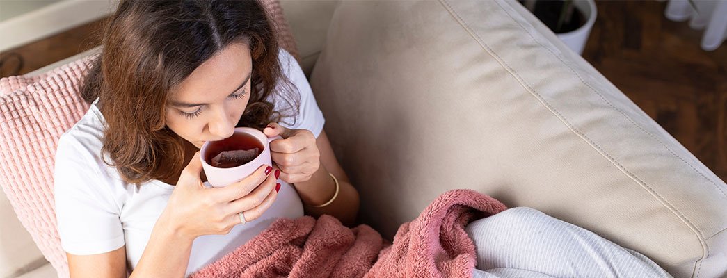 Frau mit Tee und Decke auf dem Sofa
