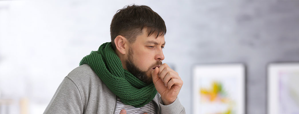 Mann mit Schal, der hustet und sich die Brust hält