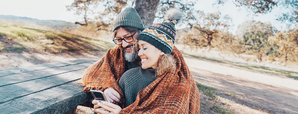 Mann und Frau sitzen gemeinsam unter einer Decke auf einer Bank im Freien