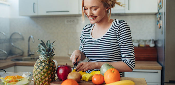 Frau steht in der Küche und schneidet Obst und Gemüse