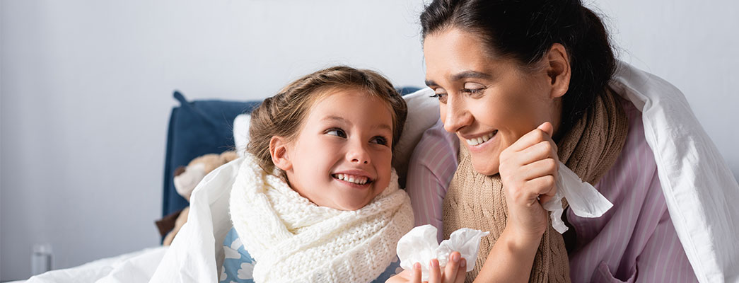 Mutter und Tochter kuscheln sich erkältet in eine Decke