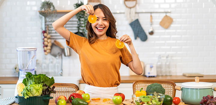 Junge Frau steht in der Küche und hält Orangenscheiben in der Hand