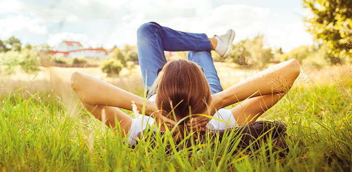 Frau liegt mit hinter dem Kopf verschränkten Armen im Gras und genießt die Sonne
