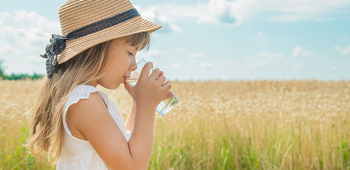 Mädchen steht im Freien und trinkt ein Glas Wasser