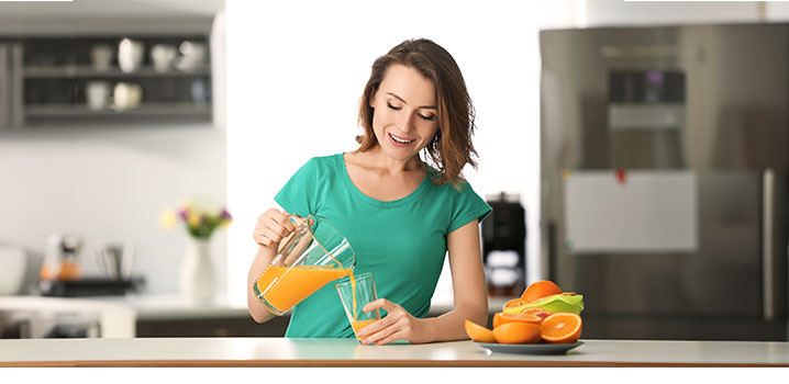 Frau steht am Küchentresten und schenkt sich Orangensaft ein