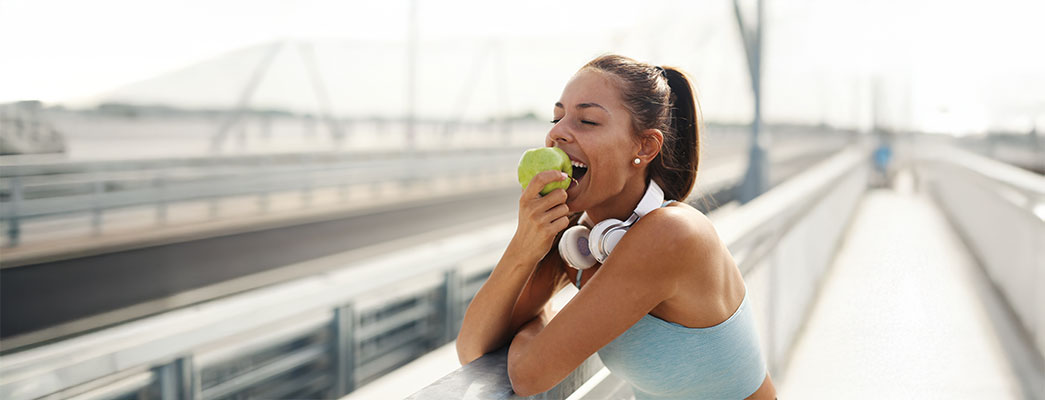 Junge Frau in Sportkleidung beißt in einen Apfel