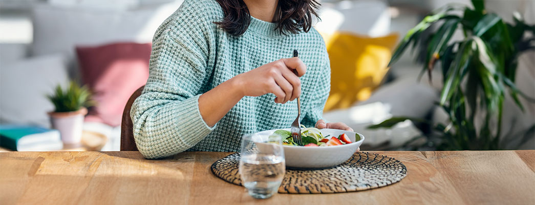 Junge Frau sitzt am Esstisch und isst einen Salat