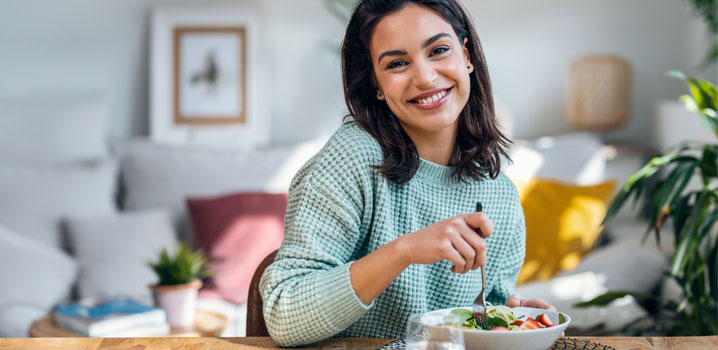 Junge Frau sitzt am Esstisch und isst einen Salat