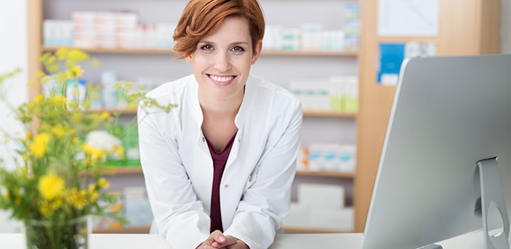 Junge Apothekerin lehnt sich auf ihrem Schreibtisch nach vorn