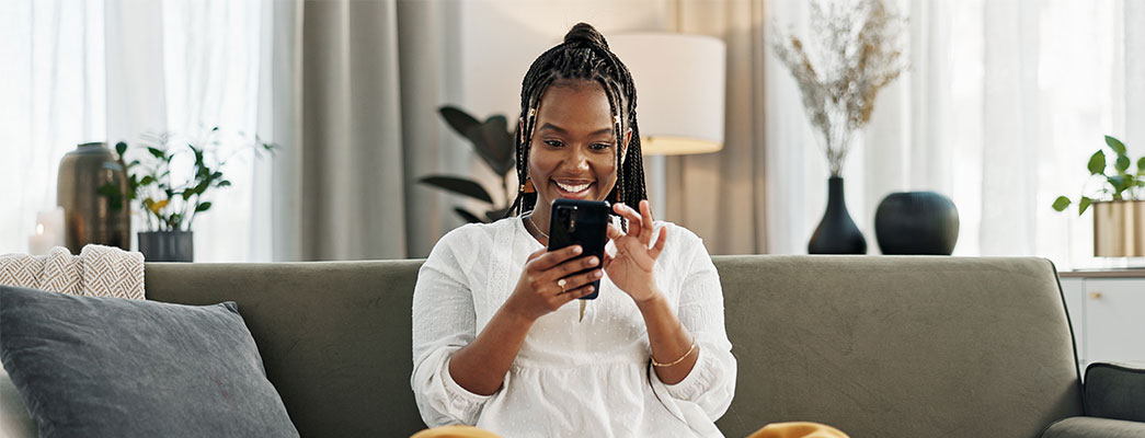 Frau die auf dem Sofa sitzt und auf dem Handy liest