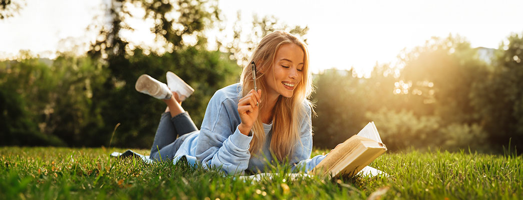 Frau die im Gras liegt und liest