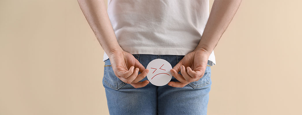 Mann in Jeans hält sich einen traurigen Smiley vor den Po