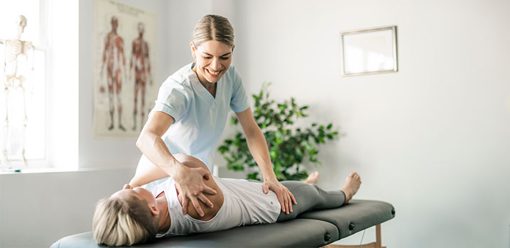 Eine Physiotherapeutin behandelt eine Frau, die auf einer Liege liegt