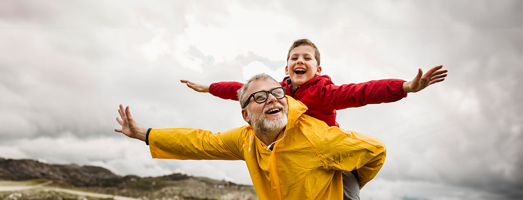 Junge sitzt auf dem Rücken seines Großvaters und streckt die Arme aus