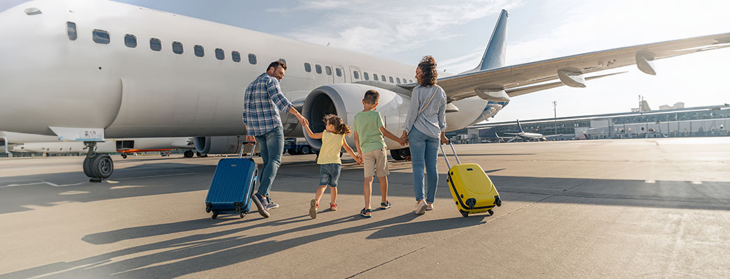 Familie mit zwei Kindern geht mit ihren Koffern auf ein Flugzeug zu