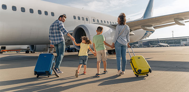 Familie mit zwei Kindern geht mit ihren Koffern auf ein Flugzeug zu