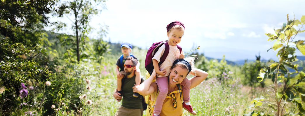 Mutter und Vater mit Kindern auf den Schultern wandern durch die Natur