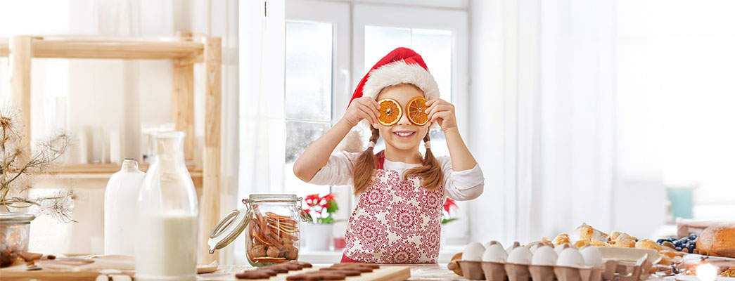 Mädchen mit Weihnachtsmütze hält sich getrocknete Orangenscheiben vor die Augen