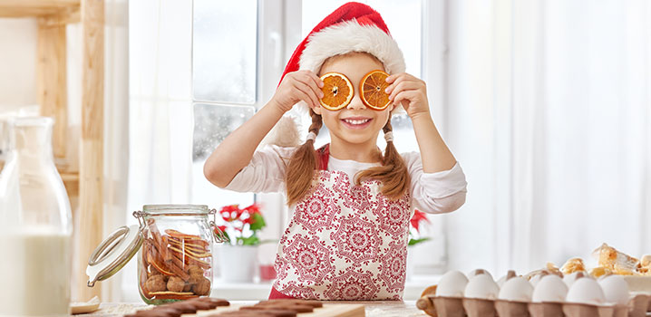 Mädchen mit Weihnachtsmütze hält sich getrocknete Orangenscheiben vor die Augen