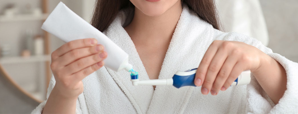 Person trägt Zahnpasta auf elektrische Zahnbürste auf